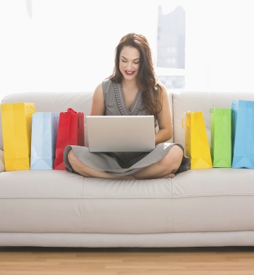 woman sitting on couch cross legged with laptop and shopping bags on either side